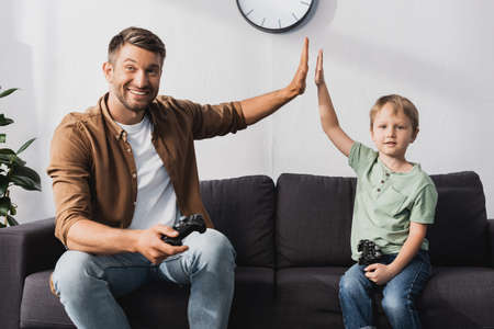 KYIV, UKRAINE - JUNE 9, 2020: cheerful father and son giving high five and looking at camera while...