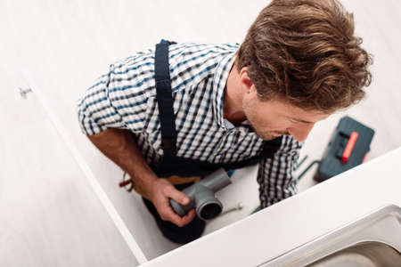 Overhead view of plumber holding plastic pipe while repairing sink near toolbox in kitchenの写真素材