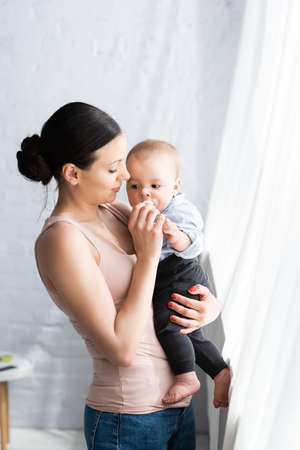 beautiful mother holding in arms barefoot infant son in baby clothingの写真素材