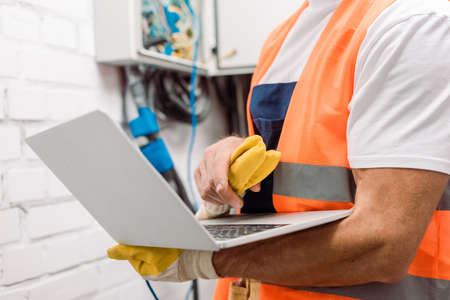 Cropped view of electrician using laptop near electrical distribution boxの写真素材