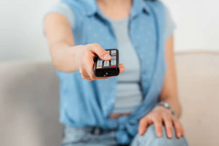 Selective focus of young woman clicking channels on couch