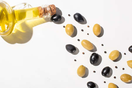 top view of olive oil in bottle near green and black olives and black pepper on white background with shadowの写真素材