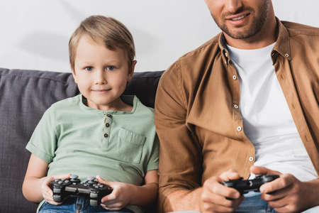 cropped view of smiling man near happy son playing video game with joystick