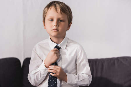 serious boy in white shirt putting tie on and looking at camera