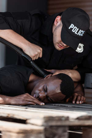 selective focus of police officer in cap with police lettering holding truncheon while detaining african american manの写真素材