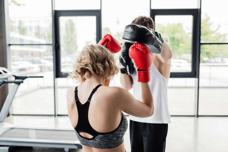 back view of sport couple in boxing gloves and pads exercising in gymの写真素材