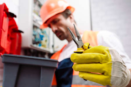 Selective focus of electrician in hardhat holding pliers near toolbox