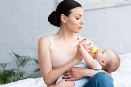 beautiful mother feeding cute infant son while holding baby bottle