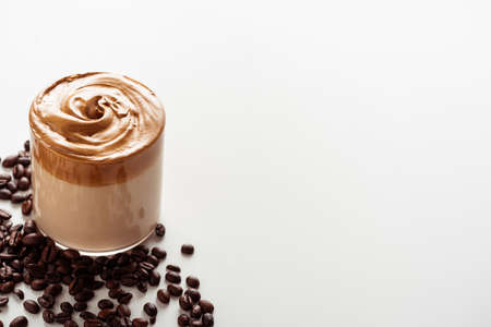 delicious Dalgona coffee in glass near coffee beans on white background