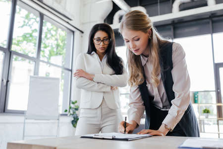 selective focus of beautiful businesswoman signing contract near woman with crossed armsの写真素材