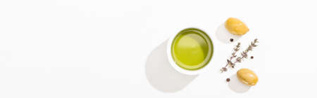 top view of olive oil in bowl near green olives, herb and black pepper on white background, panoramic orientationの写真素材