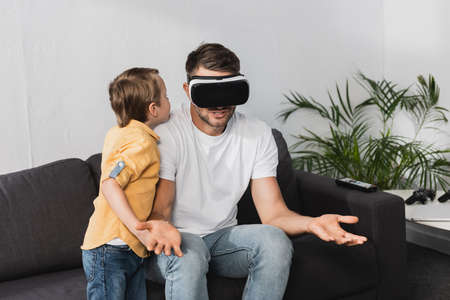 father in vr headset showing shrug gesture while cute son talking to himの写真素材