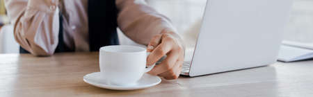 website header of businesswoman touching cup of coffee near laptopの写真素材