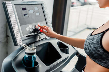 cropped view of sportswoman pointing with finger at screen on modern treadmill