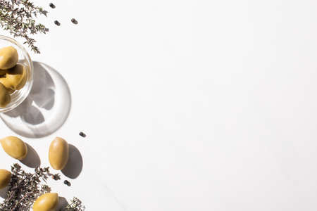 top view of green olives in bowl, herb and black pepper on white backgroundの写真素材