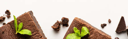 top view of delicious brownie pieces with mint and chocolate on white background, panoramic shot