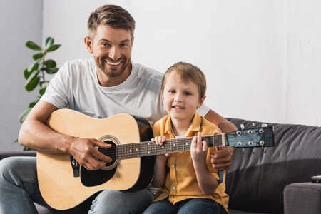 happy father teaching cheerful son how to play acoustic guitarの写真素材