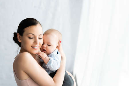 happy mother holding in arms cute infant son in baby clothingの写真素材