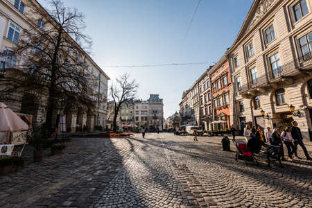 LVIV, UKRAINE - OCTOBER 23, 2019: old buildings and people walking along cafe with grand cafe...