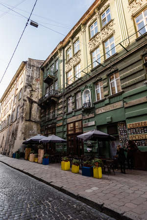 LVIV, UKRAINE - OCTOBER 23, 2019: street cafe with plants in flowerpots near old house with latin...
