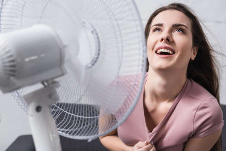 excited woman feeling comfortable with electric fan at home during summer heatの写真素材