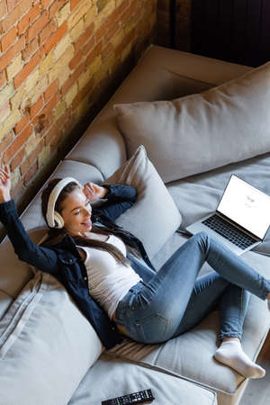 KYIV, UKRAINE - APRIL 29, 2020: overhead view of happy woman listening music in wireless headphones near laptop with google websiteのeditorial素材