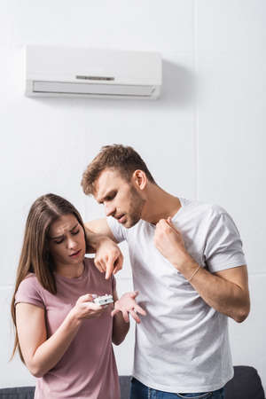 young couple suffering from heat at home with broken air conditioner