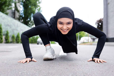 happy arabian sportswoman in hijab exercising on asphaltの写真素材