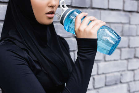 cropped view of young muslim sportswoman in hijab holding sports bottle with water outsideの写真素材