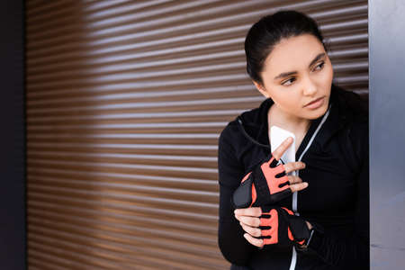 young sportswoman holding smartphone and looking away
