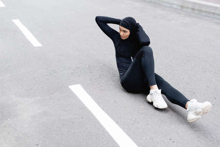 Arabian sportswoman in hijab exercising on asphaltの写真素材