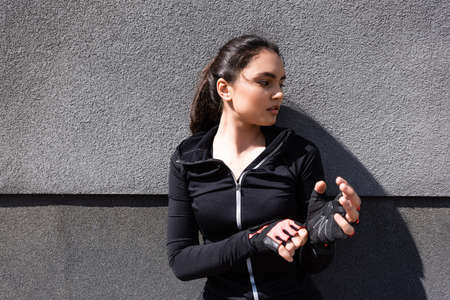 young and attractive woman touching sport gloves near concrete wall