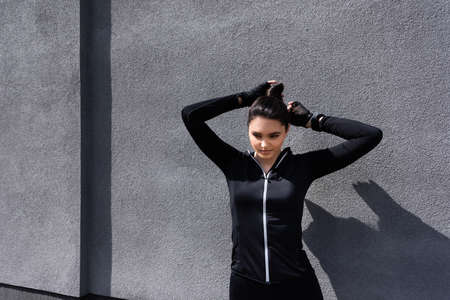 attractive sportswoman touching hair while standing near concrete wallの写真素材