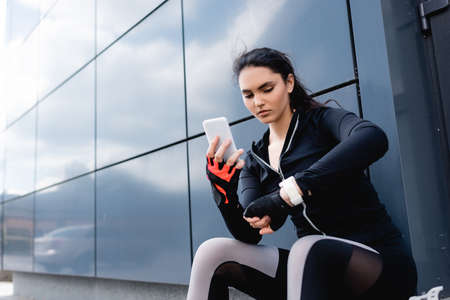 young sportswoman holding smartphone and looking at fitness trackerの写真素材