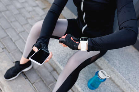 cropped view of young sportswoman with fitness tracker on hand holding smartphone with blank screenの写真素材