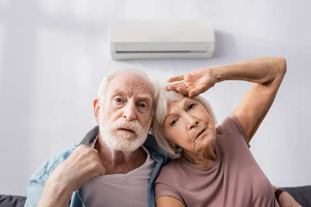Senior couple feeling hot while sitting on couch in living room