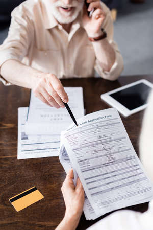 Selective focus of man talking on smartphone and pointing at papers near wife and credit card on tableの写真素材