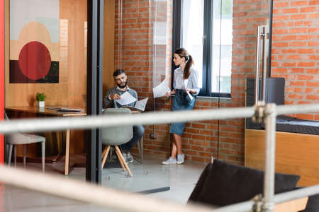 selective focus of beautiful businesswoman holding documents near man in modern officeの写真素材