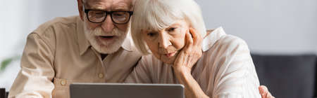 Panoramic crop of senior couple using laptop at homeの写真素材