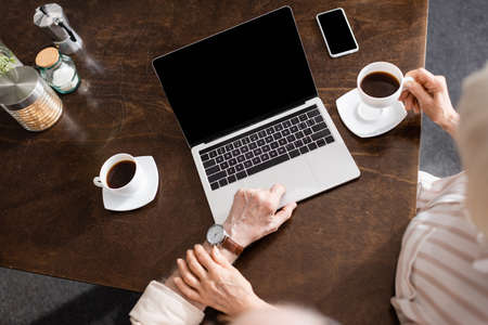 Overhead view of senior woman touching husband using laptop near coffee and smartphone on tableの写真素材