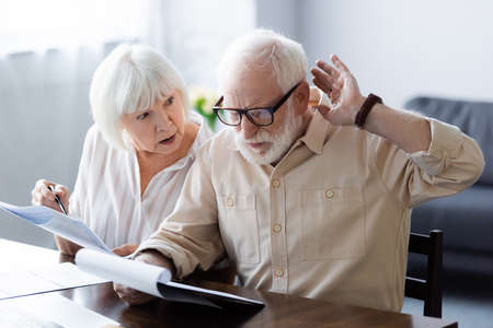 Selective focus of senior woman holding pen and documents near husband at home