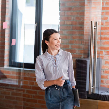 cheerful businesswoman showing thumb up in officeの写真素材
