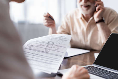 Cropped view of woman using laptop and holding papers near husband talking on smartphone at home
