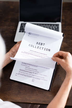 Selective focus of elderly woman holding papers with debt collection lettering near laptop on tableの写真素材