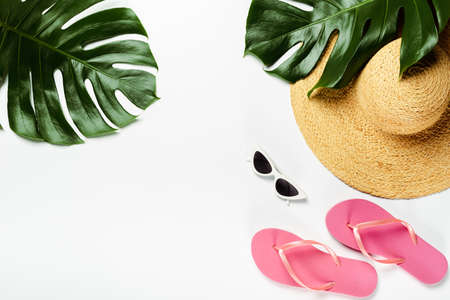 top view of green palm leaves, straw hat, sunglasses and flip flops on white background