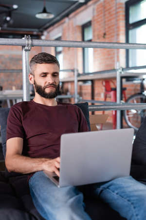 bearded businessman sitting on sofa and using laptop in office