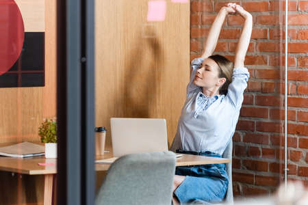 selective focus of businesswoman stretching near laptop and paper cupの写真素材