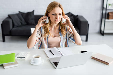 Selective focus of attractive freelancer working with laptop and headphones