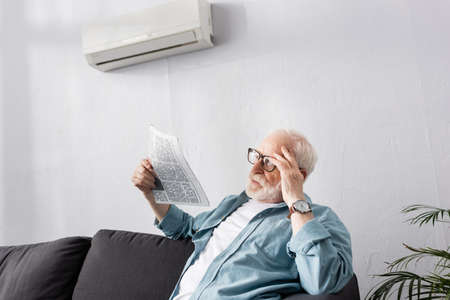 Elderly man holding newspaper on sofa at homeの写真素材
