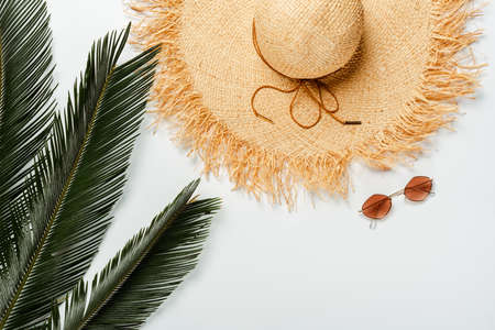 top view of green palm leaves, straw hat and sunglasses on white backgroundの写真素材